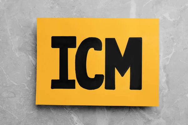 Orange paper with abbreviation ICM (International Cash Management) on light grey marble background, top view