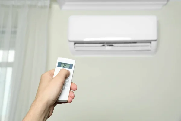 Man operating air conditioner with remote control indoors, closeup
