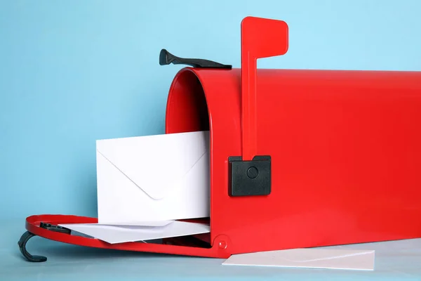 Open red letter box with envelopes on turquoise background, closeup