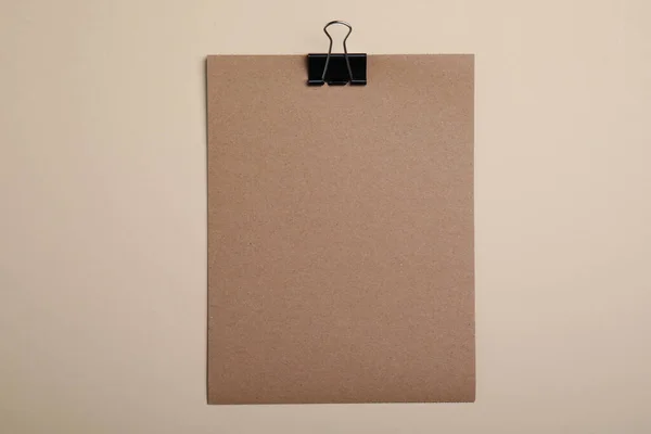 Sheet of brown paper with clip on beige background, top view