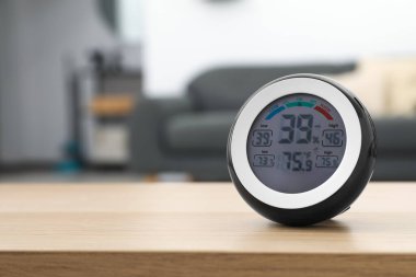 Digital hygrometer with thermometer on wooden table in room. Space for text
