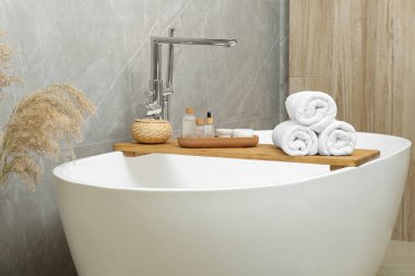 Rolled bath towels and personal care products on tub tray in bathroom