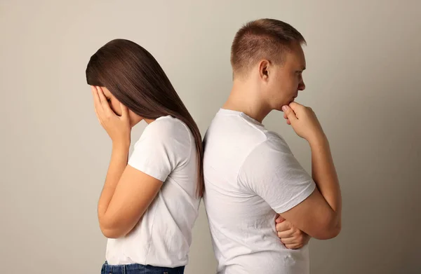 Unhappy young couple turning their backs on each other against light background