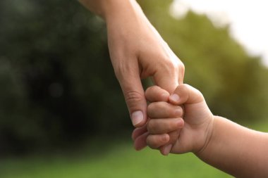 Kızı, parkta annesinin elini tutuyor, yakın plan. Mutlu aile