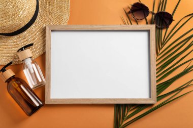 Boş fotoğraf çerçevesi, hasır şapka, kozmetik, güneş gözlüğü ve turuncu arka planda tropikal yaprak, düzlük