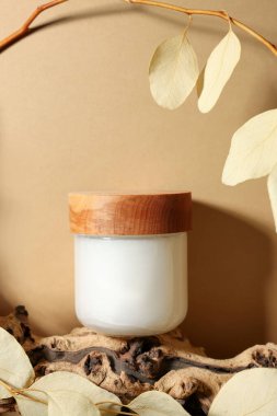 Jar of luxury cream and dried leaves on dark beige background