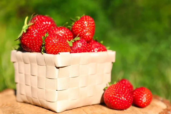 Basket and ripe strawberries on tree stump outdoors, closeup