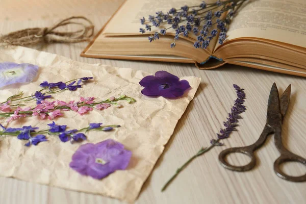 Beautiful dried flowers, book and scissors on wooden table, closeup