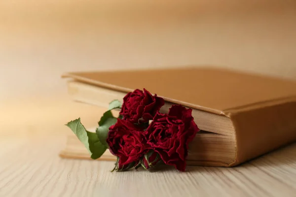 Beautiful dried flowers in book on wooden table, closeup