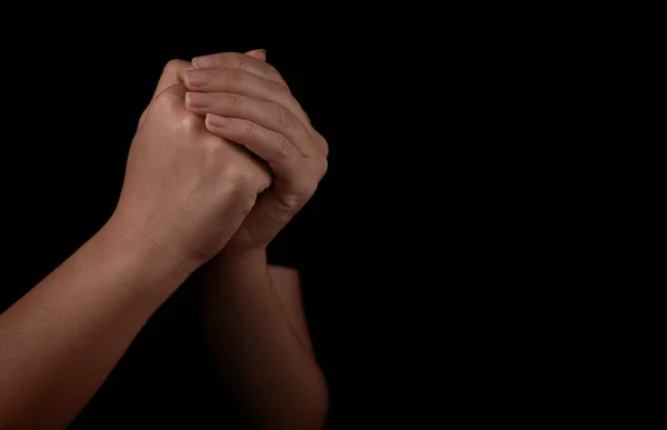 Woman holding hands clasped while praying against black background, closeup. Space for text