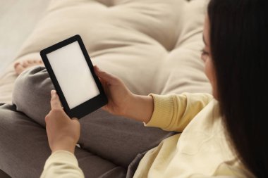 Kanepede e-kitap okuyan genç bir kadın, yakın plan.