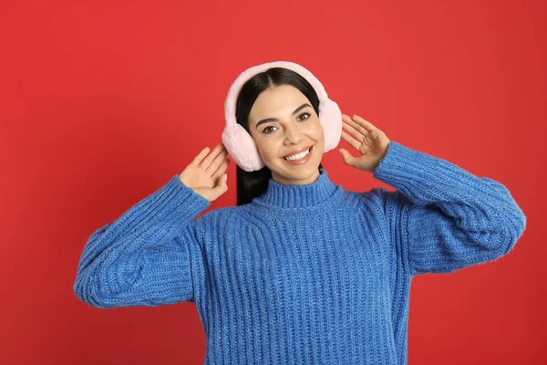 美しいです若いです女性身に着けていますEarmuff上の赤い背景 — ストック写真