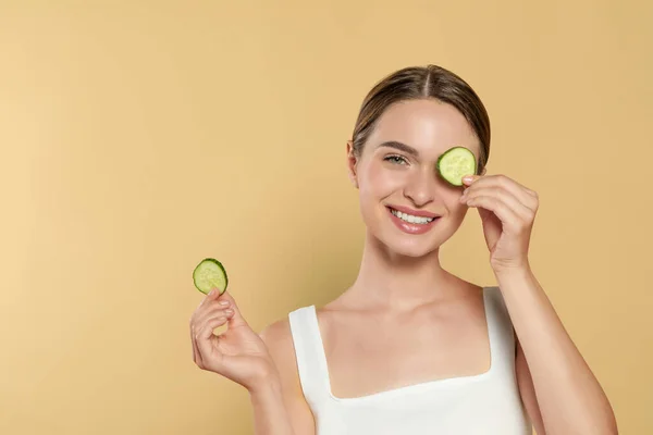 Young woman with cucumber slices on beige background, space for text. Eye skin care