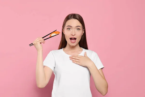 Emotionale Junge Frau Hält Sushi Mit Essstäbchen Auf Rosa Hintergrund — Stockfoto