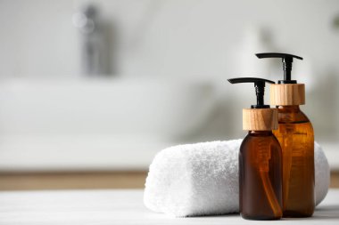 Kişisel bakım ürünleri ve banyodaki beyaz ahşap masaya sarılmış havlu, yakın plan. Metin için boşluk