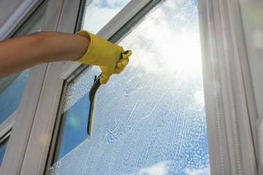 Woman cleaning glass with squeegee indoors, closeup