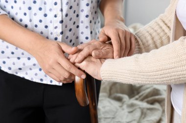 Caregiver and elderly woman with walking cane at home, closeup