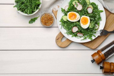 Delicious salad with boiled egg, vegetables and arugula served on white wooden table, flat lay. Space for text