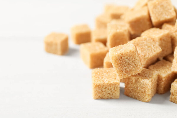 Heap of brown sugar cubes on white table, closeup. Space for text