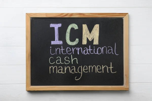Small blackboard with abbreviation ICM (International Cash Management) on white wooden background, top view