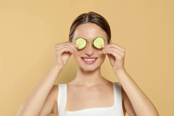 Young woman with cucumber slices on beige background. Eye skin care