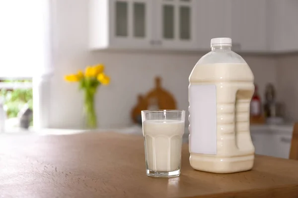 Gallon bottle of milk and glass on wooden table in kitchen. Space for text