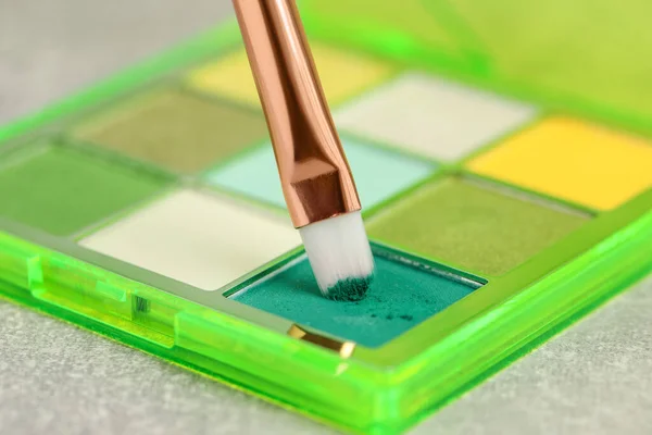 Colorful eyeshadow palette with brush on grey table, closeup