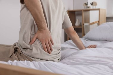 Yatakta otururken sırt ağrısı çeken bir adam, yakın plan. Skolyoz belirtileri