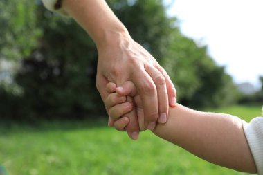Kızı, parkta annesinin elini tutuyor, yakın plan. Mutlu aile