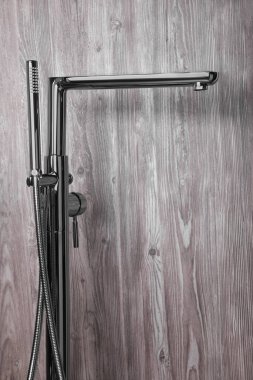 Ahşap arka planda el banyosu olan modern banyo musluğu.
