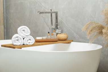 Rolled bath towels and personal care products on tub tray in bathroom