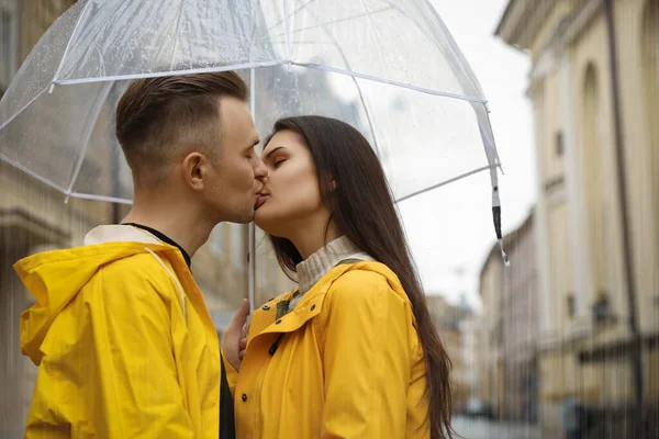 Lovely young couple with umbrella kissing on city street