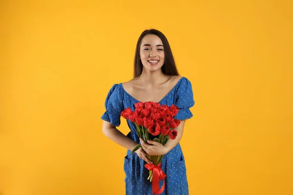 Happy woman with red tulip bouquet on yellow background. 8th of March celebration