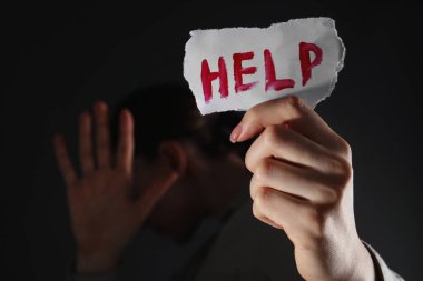 Elinde kelime olan bir kağıt parçası olan bir kadın. Siyah arka planda yardım, yakın plan. Aile içi şiddet kavramı