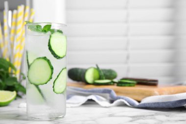 Glass of refreshing cucumber water with mint on white marble table, space for text