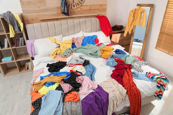 Pile of clothes on bed in messy room. Fast fashion concept