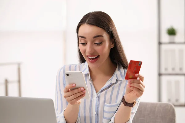 Woman with credit card using smartphone for online shopping indoors