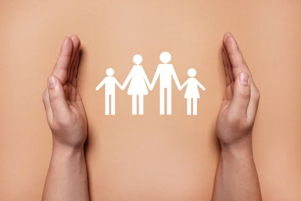 Man holding hands around paper silhouette of family on coral background, top view. Insurance concept