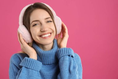Mutlu kadın pembe arka planda sıcak kulaklık takıyor, mesaj için yer var.