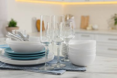 Different clean dishware, cutlery and glasses on white table in kitchen