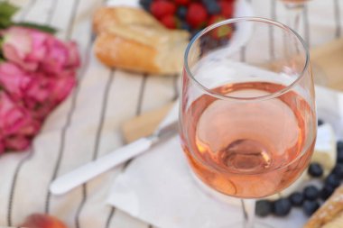 Glass of delicious rose wine and food on white picnic blanket, closeup