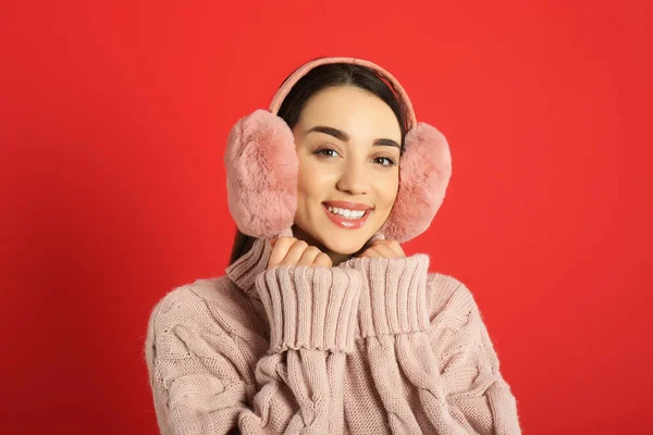 美しいです若いです女性身に着けていますEarmuff上の赤い背景 — ストック写真