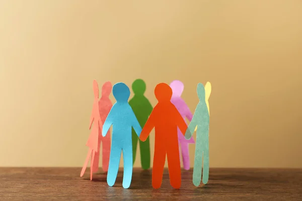 Many different paper human figures standing in circle on wooden table against beige background. Diversity and inclusion concept