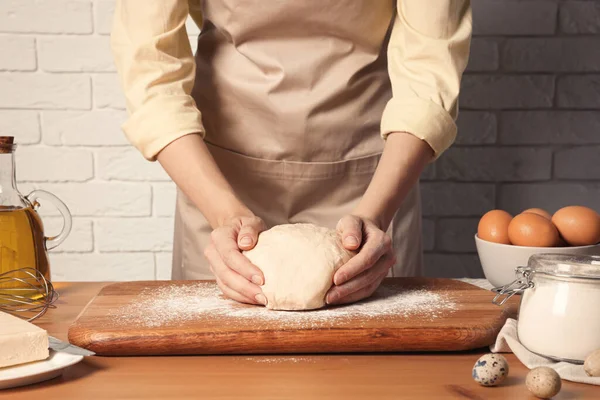 Beyaz tuğla duvarın yanındaki ahşap masada hamur yoğuran kadın, yakın plan.