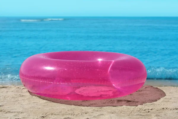 Bright inflatable ring on sandy beach near sea