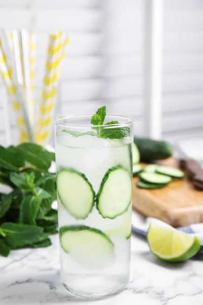 Glass of refreshing cucumber water with mint on white marble table