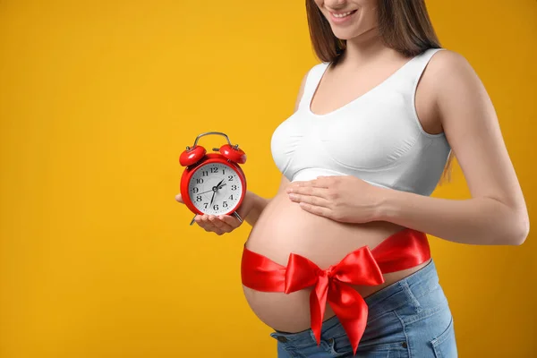 Jonge Zwangere Vrouw Met Wekker Rode Strik Gele Achtergrond Close — Stockfoto