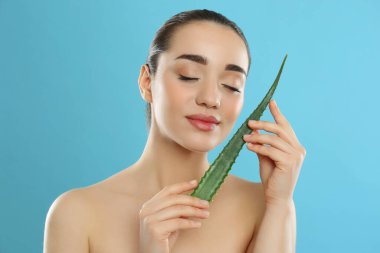 Açık mavi arka planda aloe vera yaprağı olan genç bir kadın.