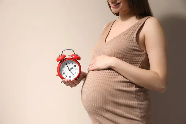 ベージュの背景に腹の近くに目覚まし時計を持っている若い妊婦は テキストのためのクローズアップとスペース 出産までの時間 — ストック写真