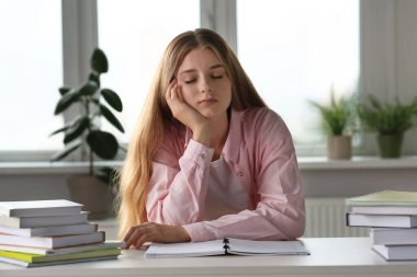 Beyaz masada kitapların yanında uyuyan genç, yorgun bir kadın.